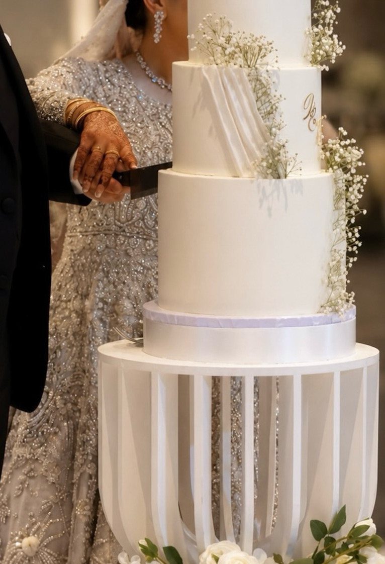 Couple cutting a multi-tiered white wedding cake decorated with baby's breath flowers.