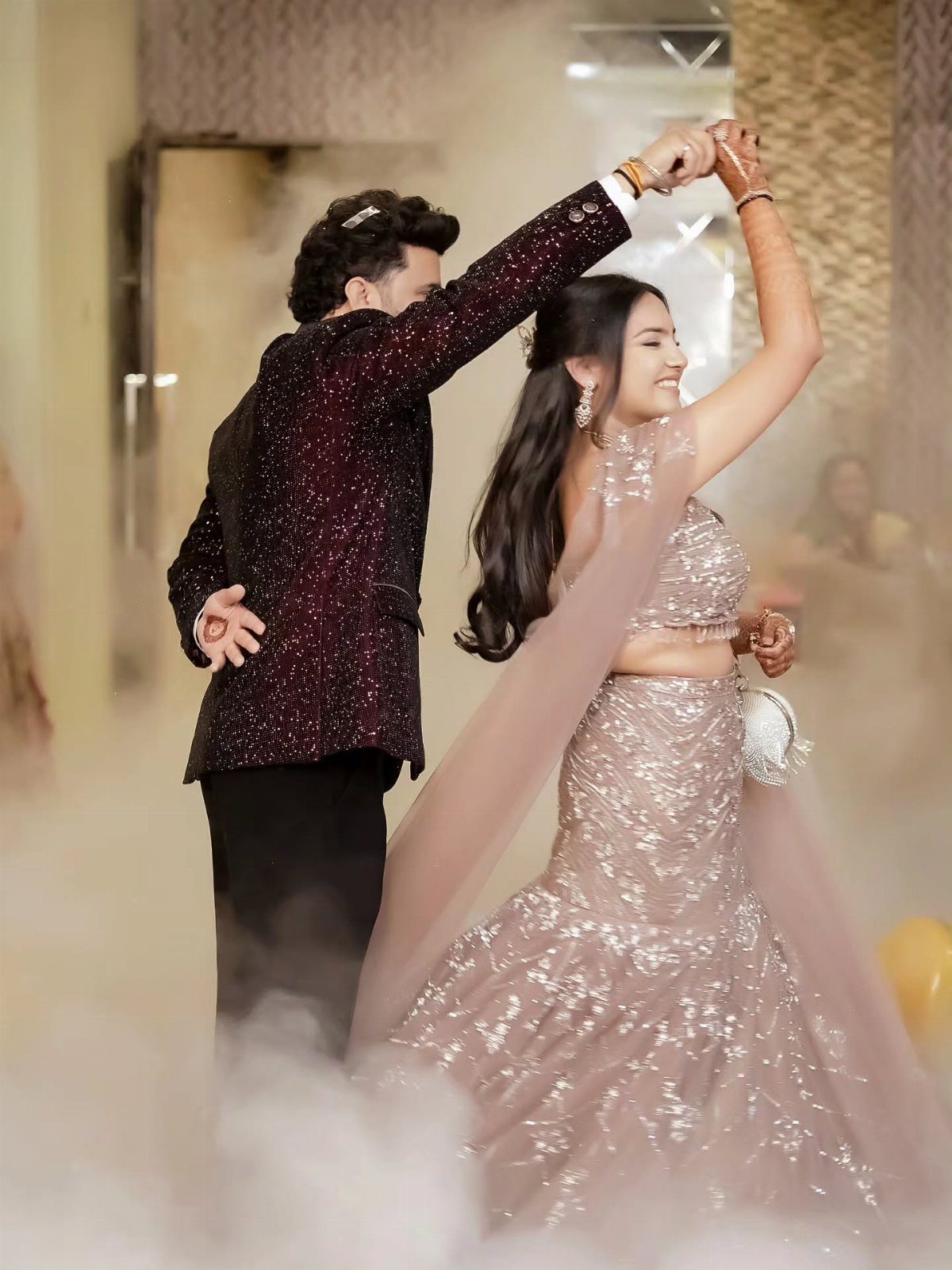 Couple dancing together in a fog-filled room wearing shimmering wedding attire.