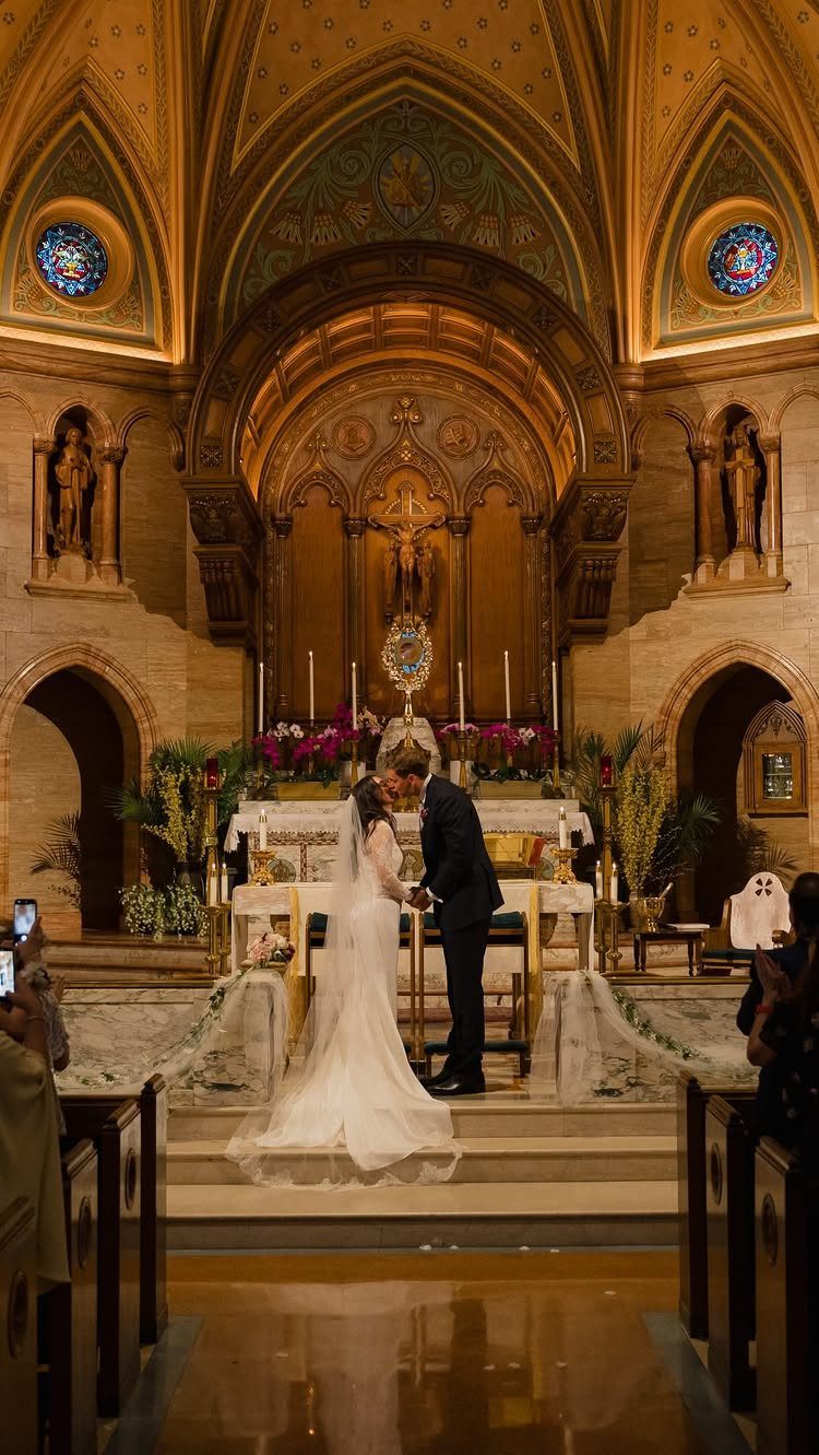 Bride and groom kissing at the altar inside a grand, ornate cathedral.