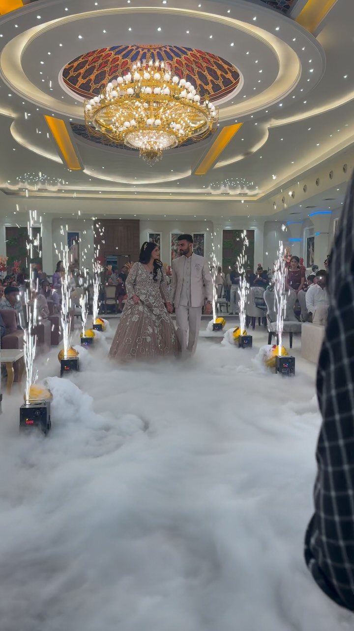Bride and groom walking through white fog with sparklers in a ballroom