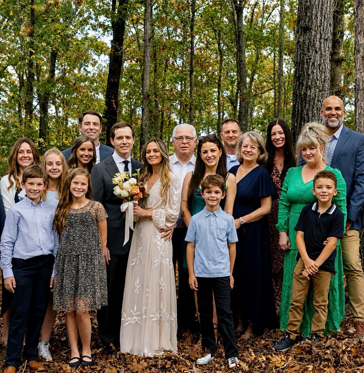 Wedding party and family posing for a group portrait in an autumn forest.