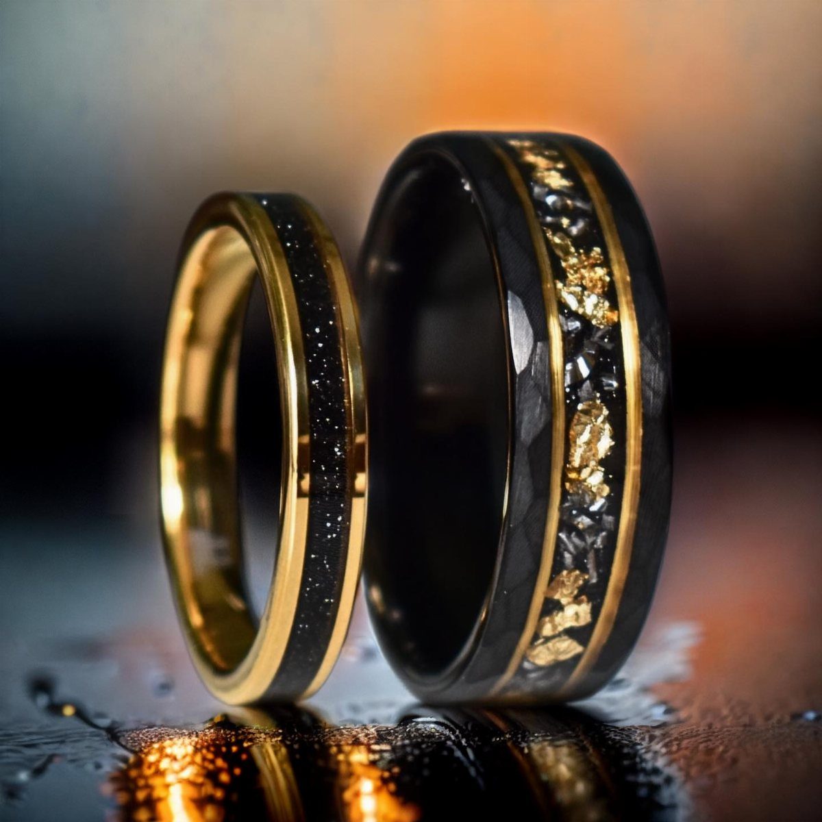 Two black and gold wedding bands resting on a dark reflective wet surface