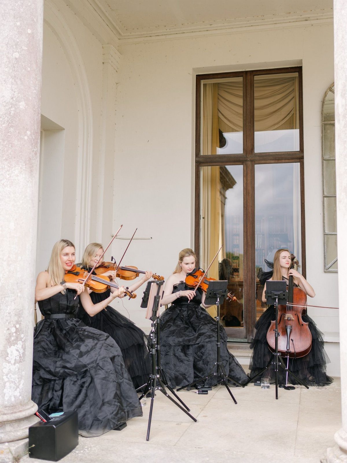 String quartet in black gowns playing violins and cello on a stone patio.