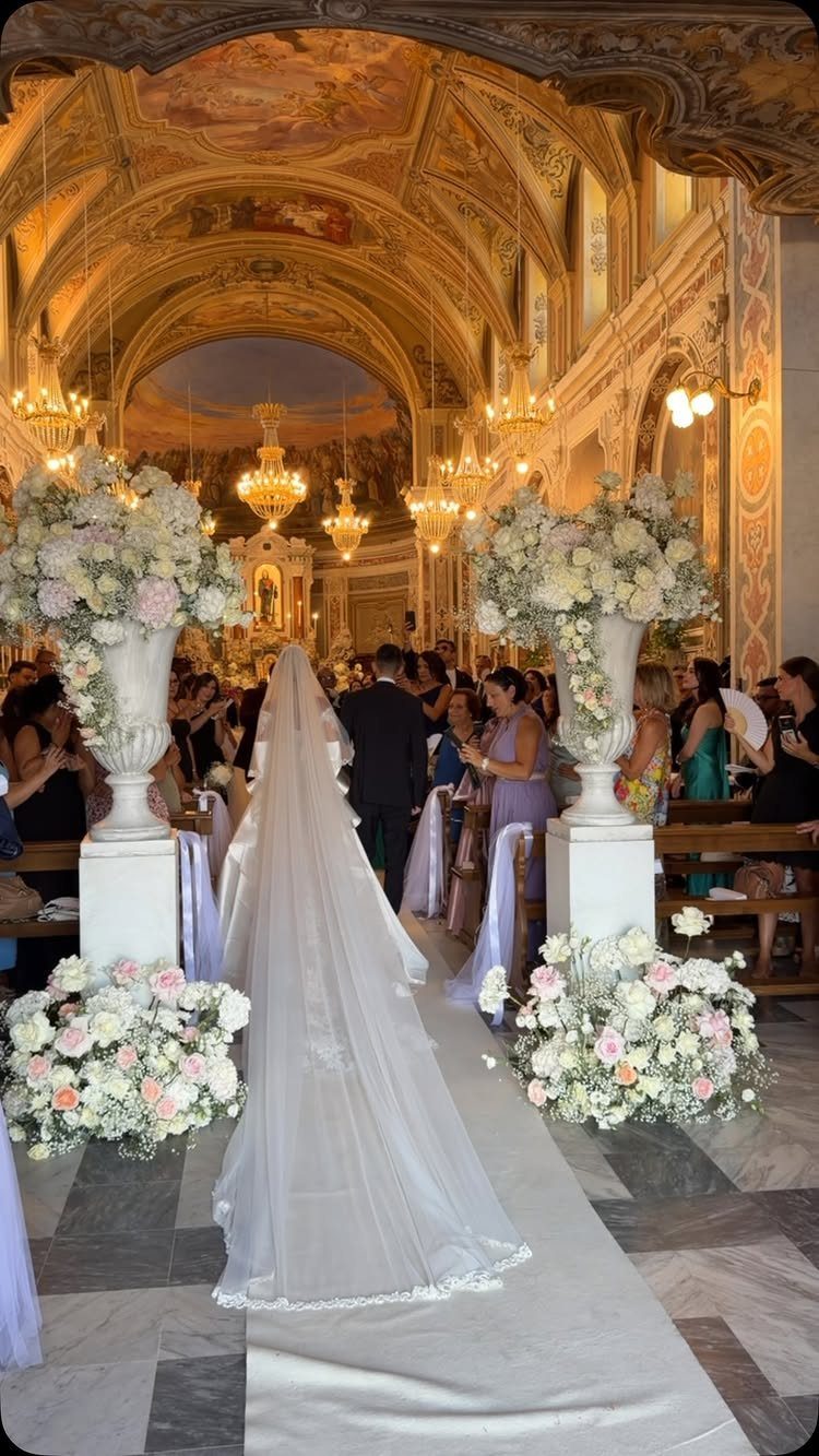 Bride with long veil walking down the aisle in an ornate church