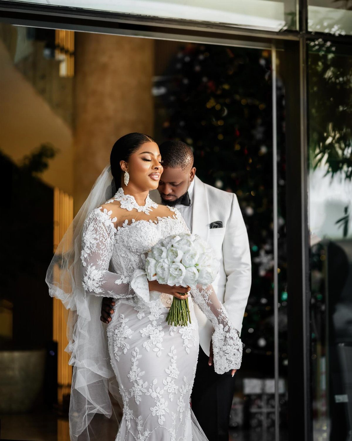Bride in lace gown and groom in white tuxedo posing for an intimate portrait.