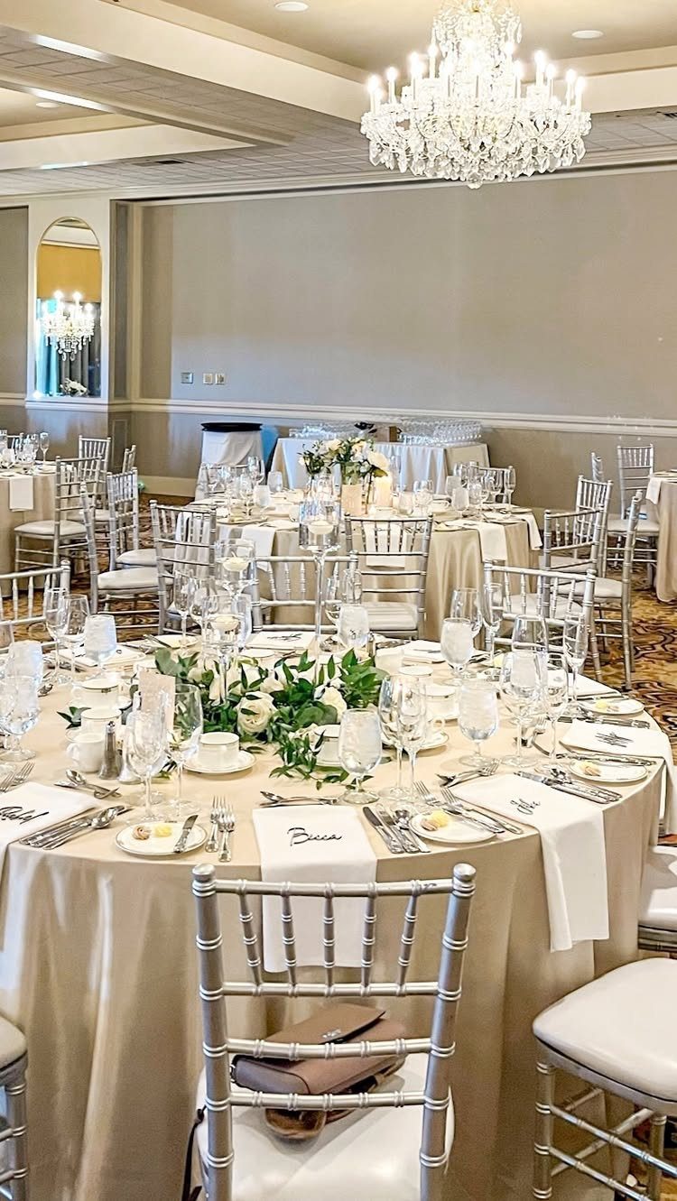 Wedding reception tables with champagne linens, greenery centerpieces, and crystal chandeliers above.