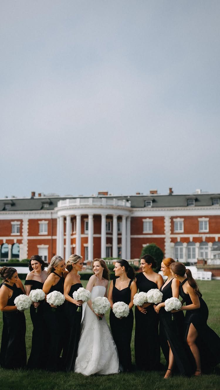 Bride in white gown posing with bridesmaids in black dresses holding white bouquets.