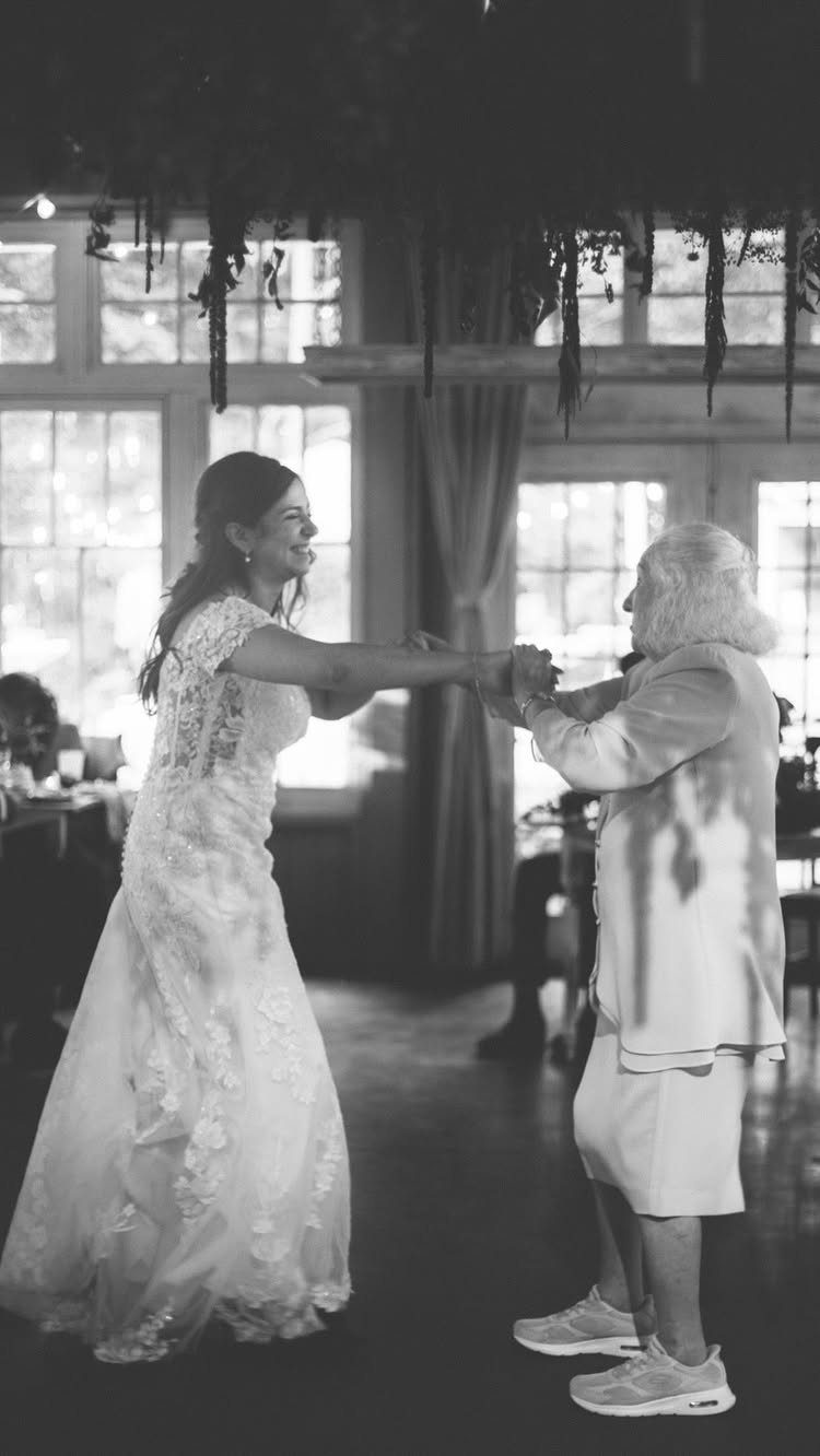 Bride in lace gown dancing with an elderly woman in a light suit.