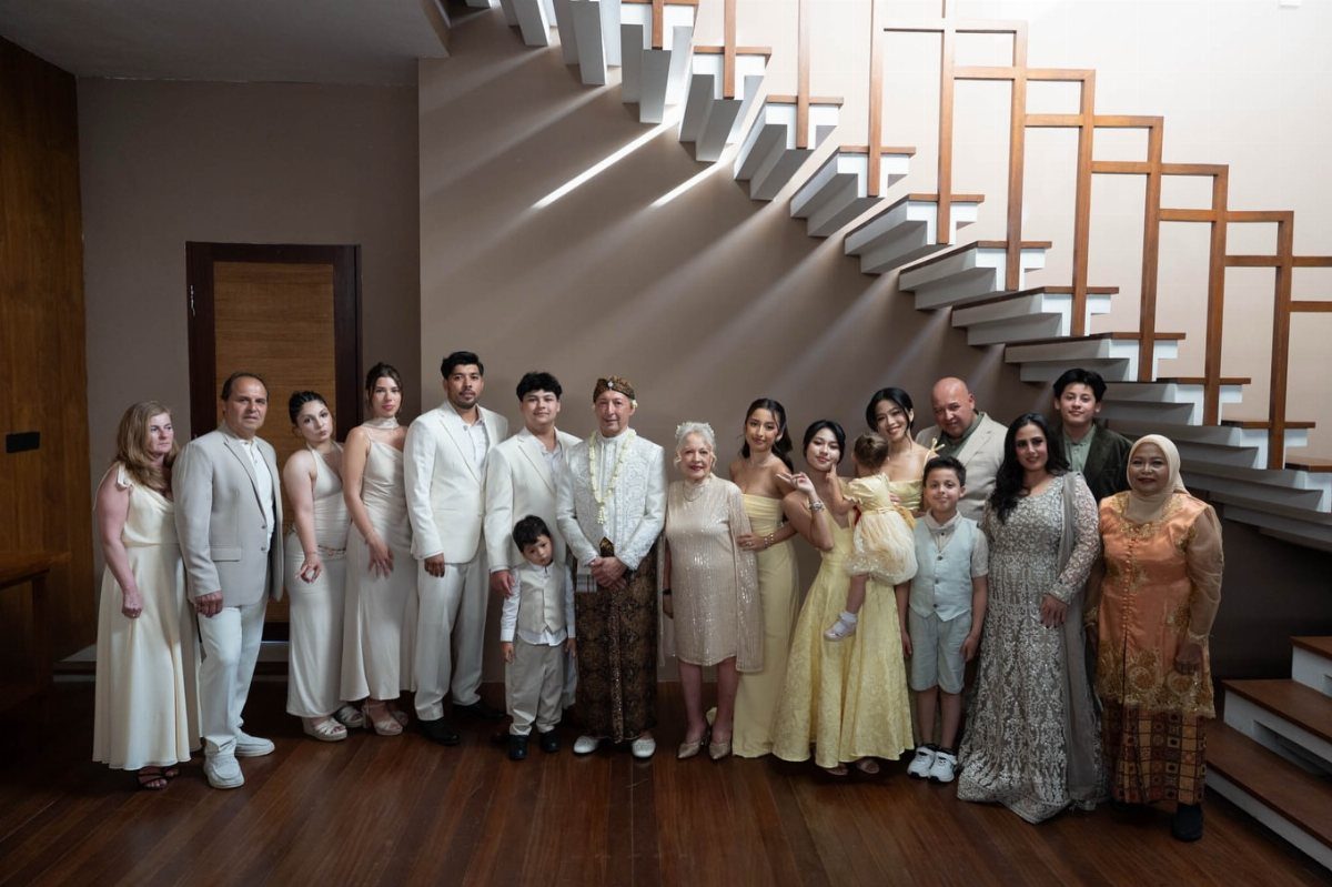 Large family group in formal white and gold clothing posing by a staircase.