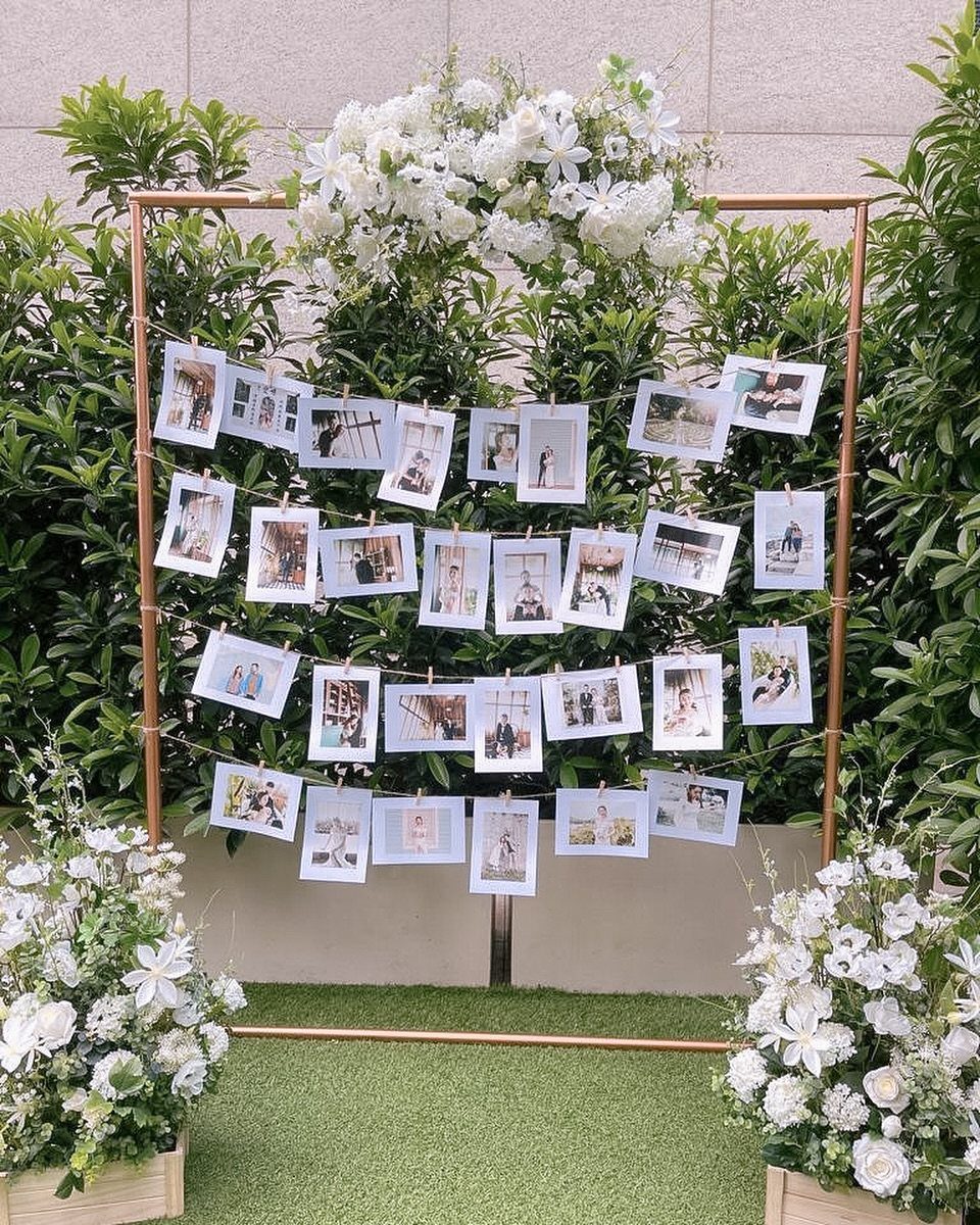 Gold frame with white flowers displaying family photographs clipped to strings against greenery