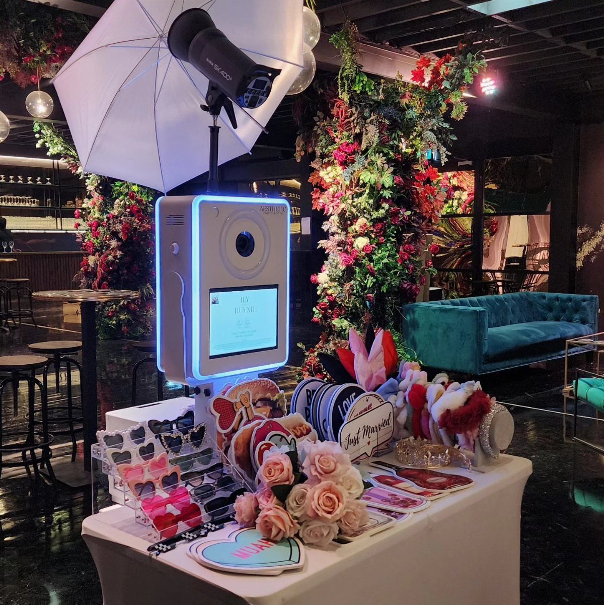 Digital photo booth kiosk with props and photography lighting in a floral venue