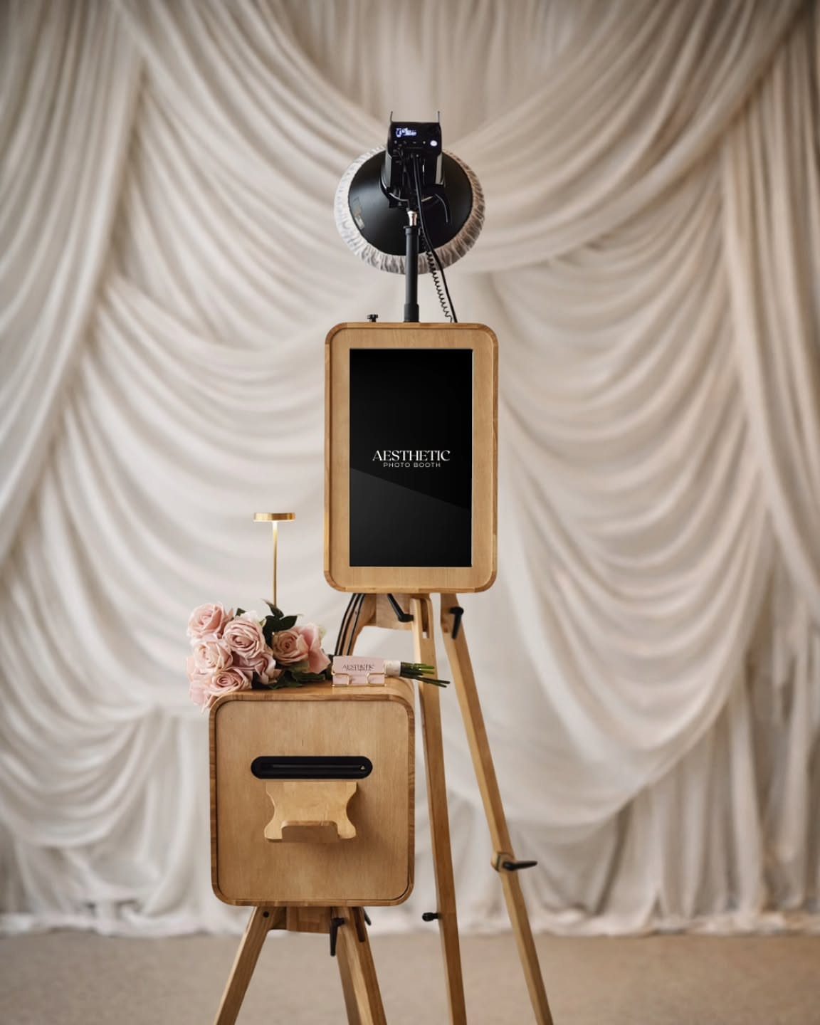 Digital photo booth with wooden frame and studio light against white draped fabric