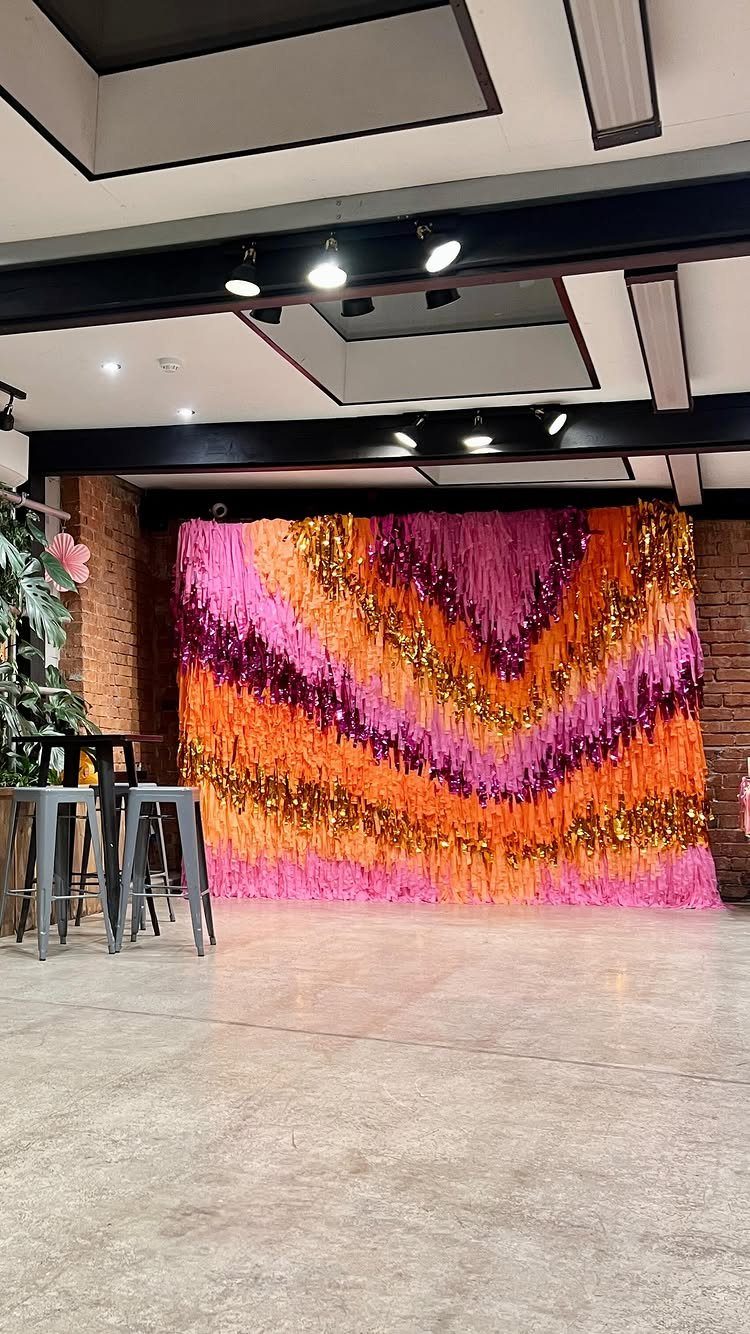 Colorful pink, orange, and gold streamer wall backdrop in a modern indoor space.