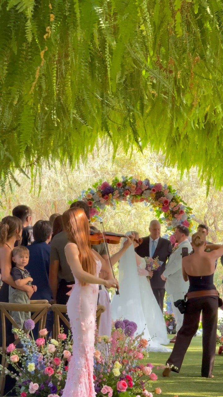 Female violinist playing during an outdoor wedding ceremony under a floral arch