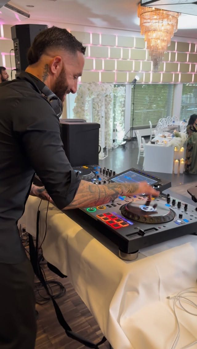 DJ with tattoos operating a controller at a wedding reception event