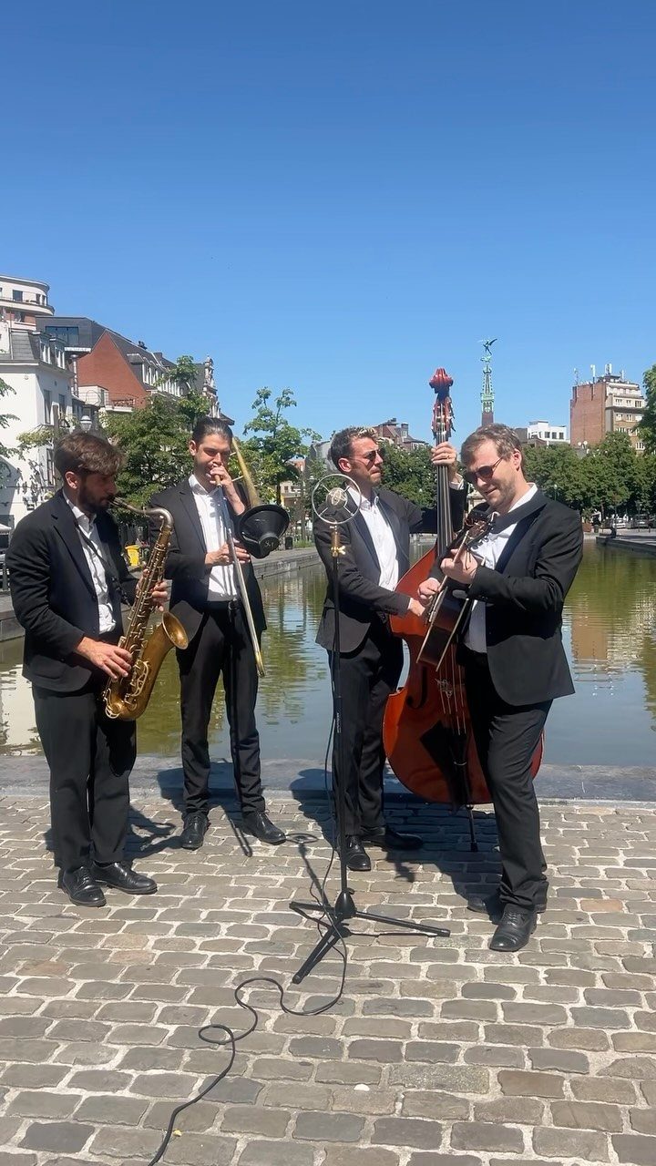 Four musicians in tuxedos playing saxophone, trombone, trumpet, and double bass outdoors.