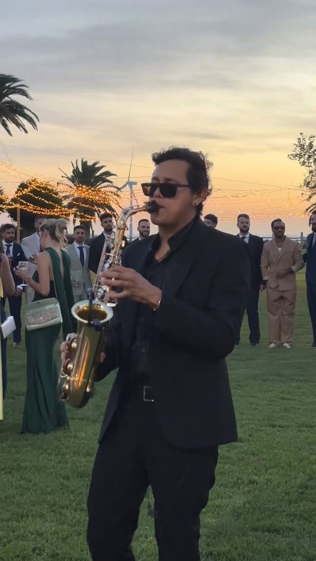 Musician in a black suit playing a saxophone at an outdoor wedding reception.