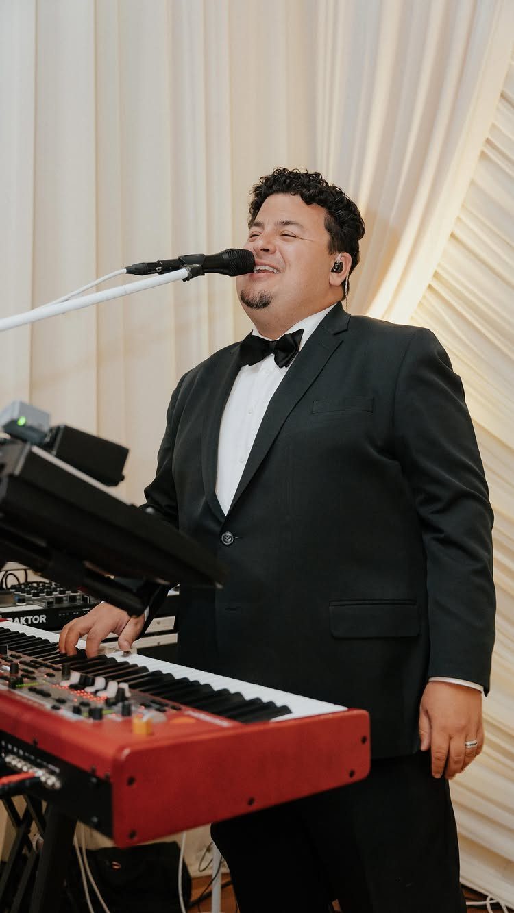 Male singer in a tuxedo performing with a red keyboard and microphone.