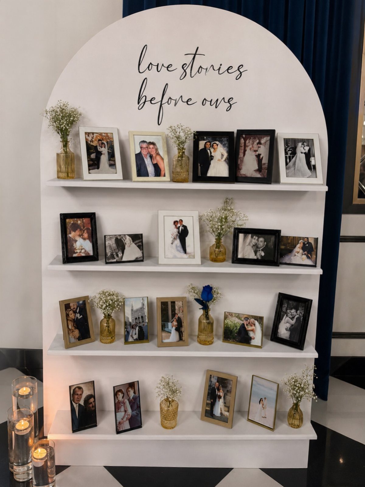 White arched shelving unit displaying framed wedding photos and small floral arrangements.