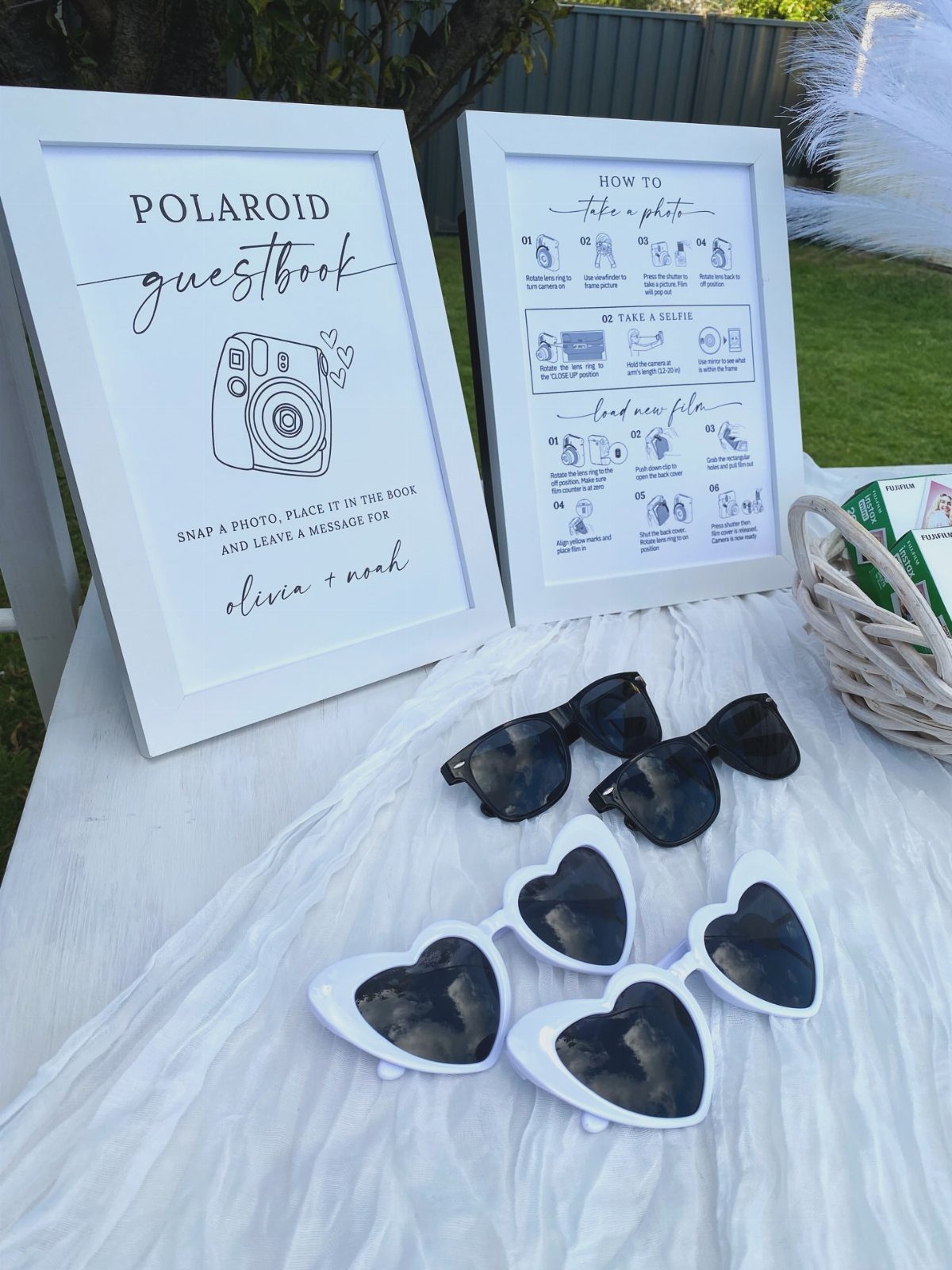 Polaroid guestbook signs and heart-shaped sunglasses on a white cloth covered table.