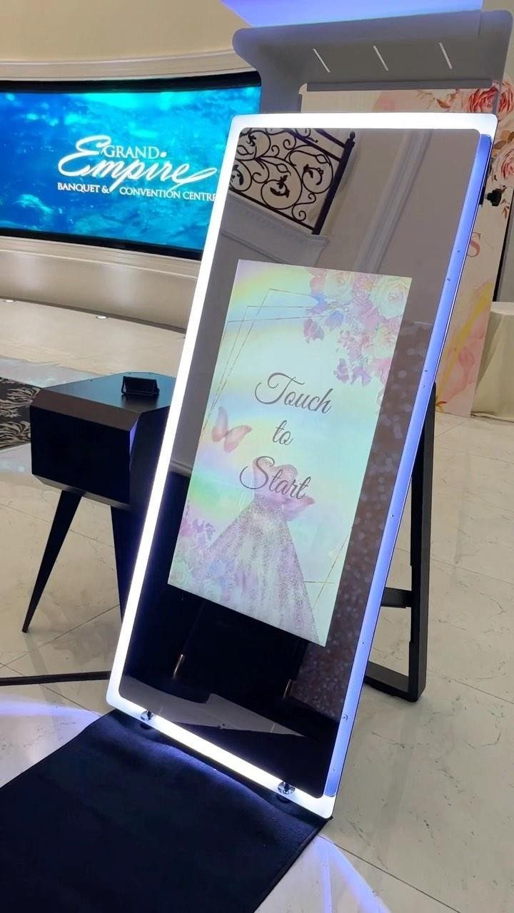 Interactive mirror photo booth with a glowing white frame and touch screen interface.