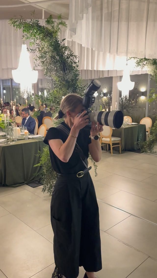 Photographer with professional camera capturing moments at a wedding reception with greenery.