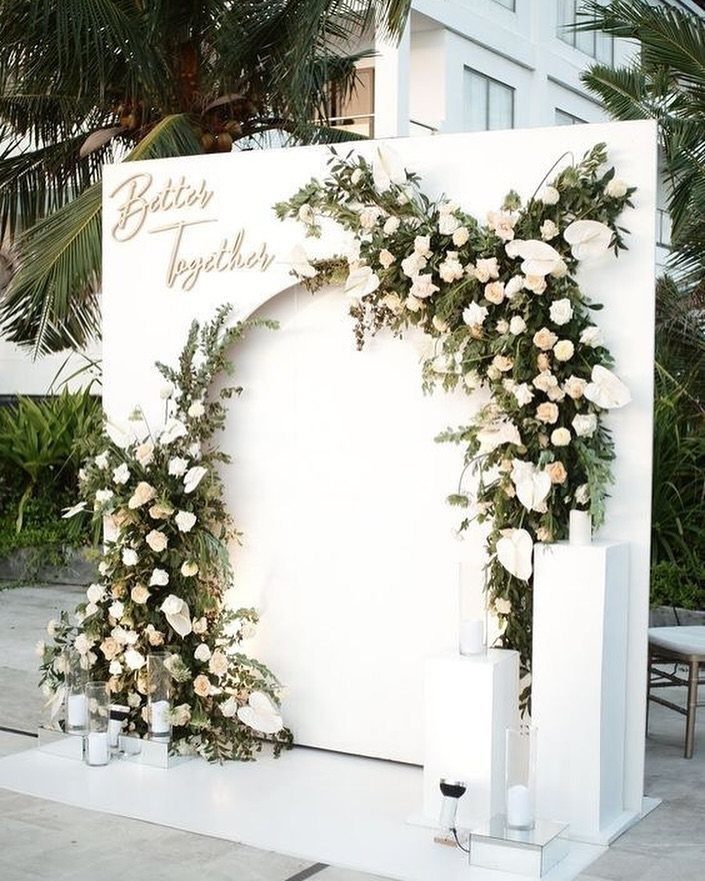White floral backdrop with gold Better Together text and white pedestals outdoors