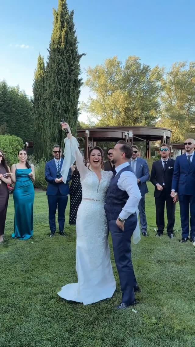 Bride and groom laughing together on a lawn surrounded by wedding guests.