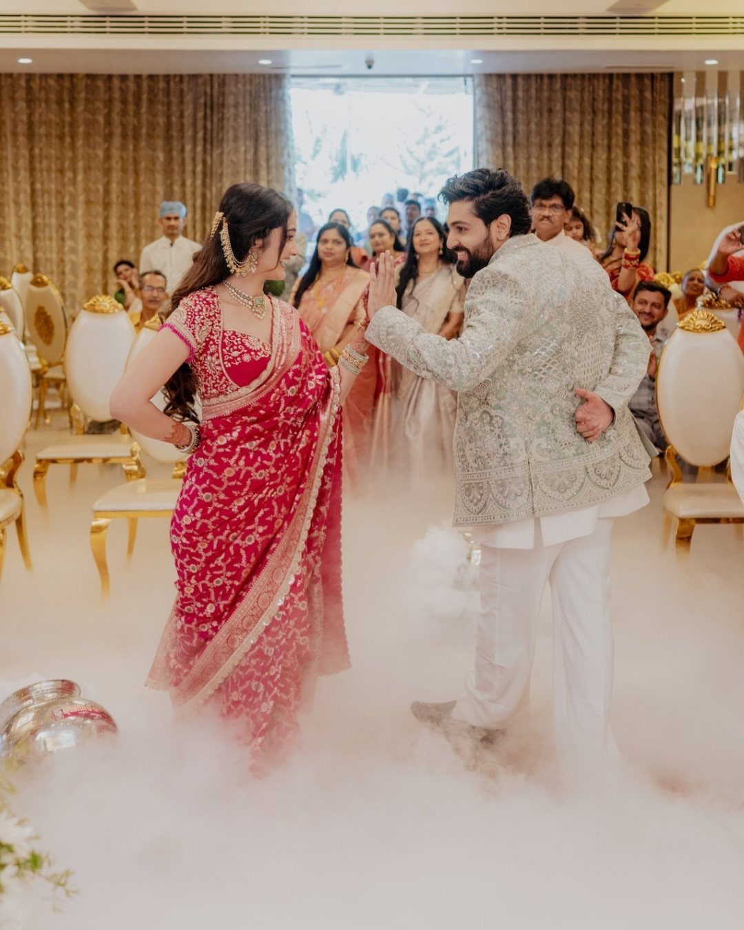 Bride in red saree and groom in white sherwani facing each other in fog
