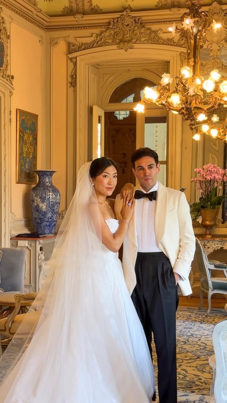 Bride and groom posing together in an ornate room with a gold chandelier.