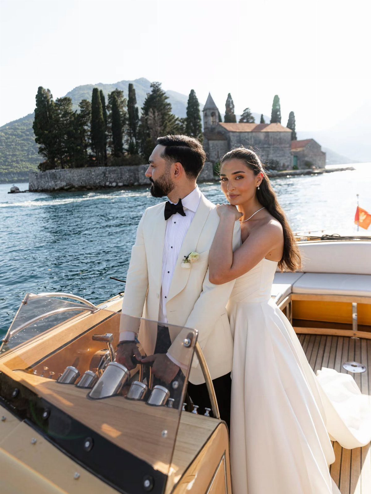 Bride and groom posing on a wooden boat with a coastal island background