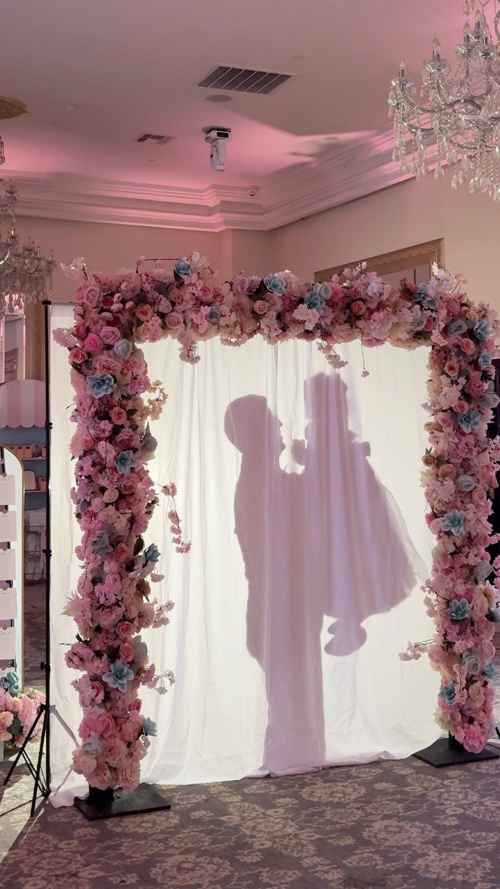 Silhouette of a bride and groom projected on a white floral wedding backdrop