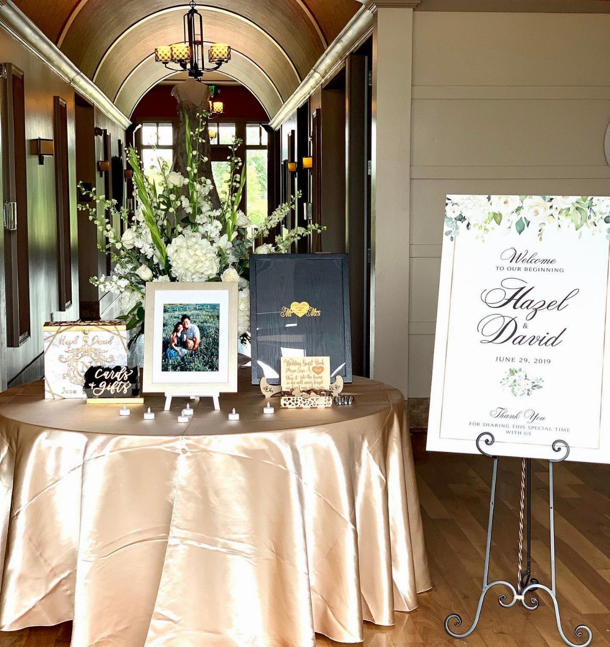 Champagne satin welcome table with framed photo, white flowers, and a welcome sign.