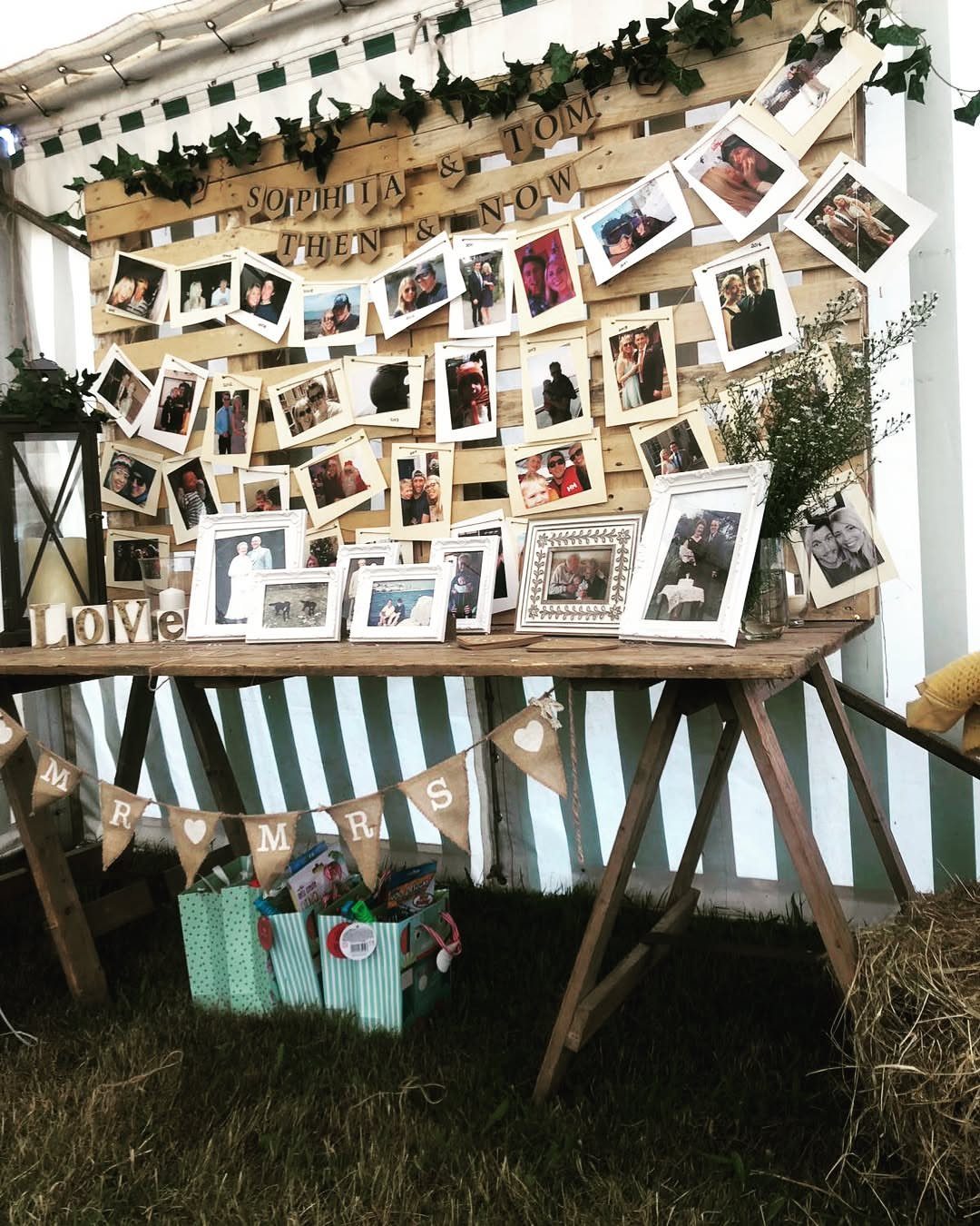 Wooden pallet backdrop displaying numerous wedding photos behind a rustic trestle table.