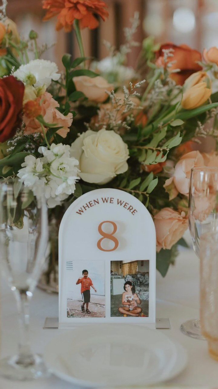 Arched table number card with childhood photos and a colorful floral centerpiece.