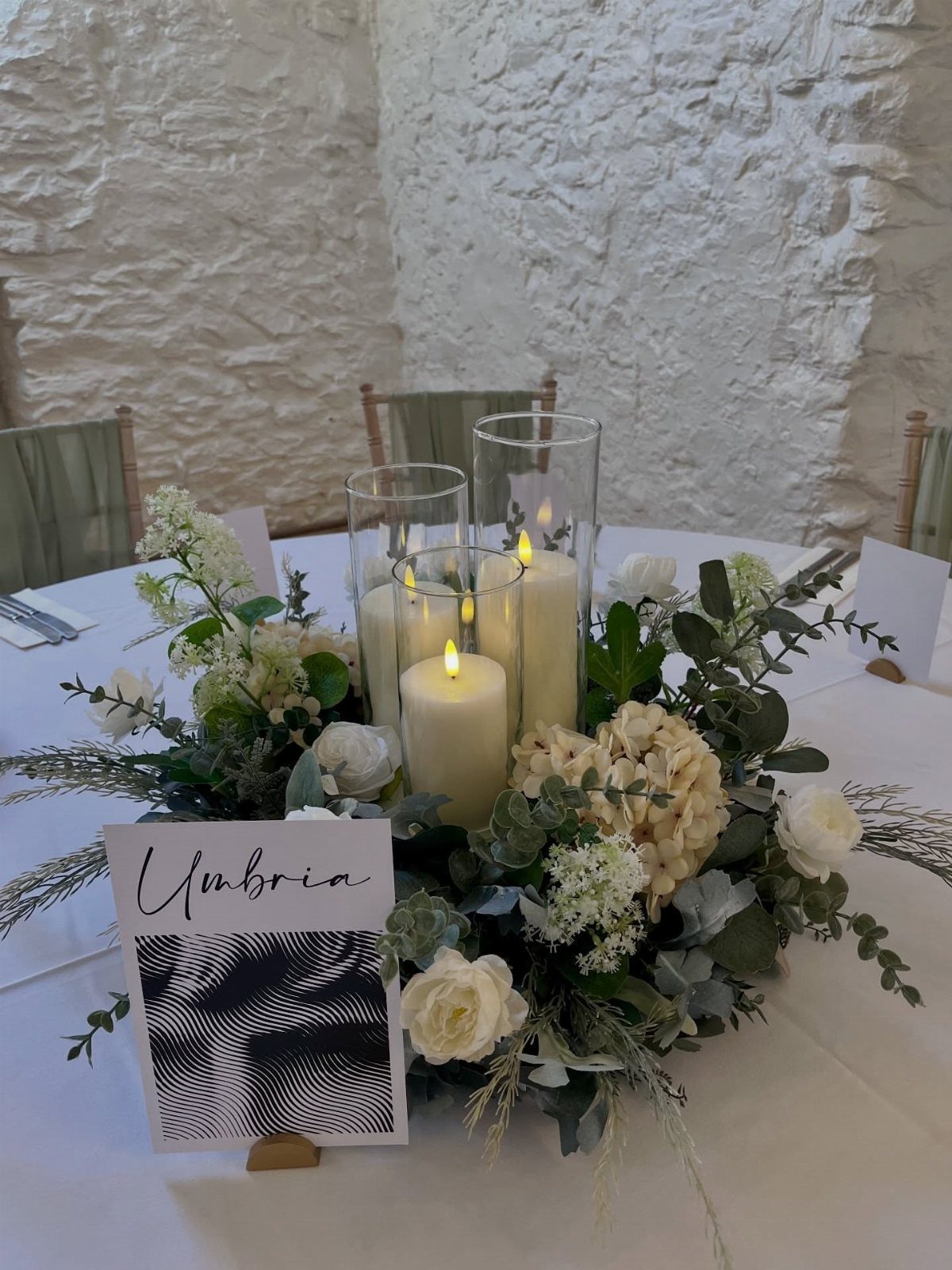 Floral centerpiece with lit pillar candles and a table name card on white tablecloth