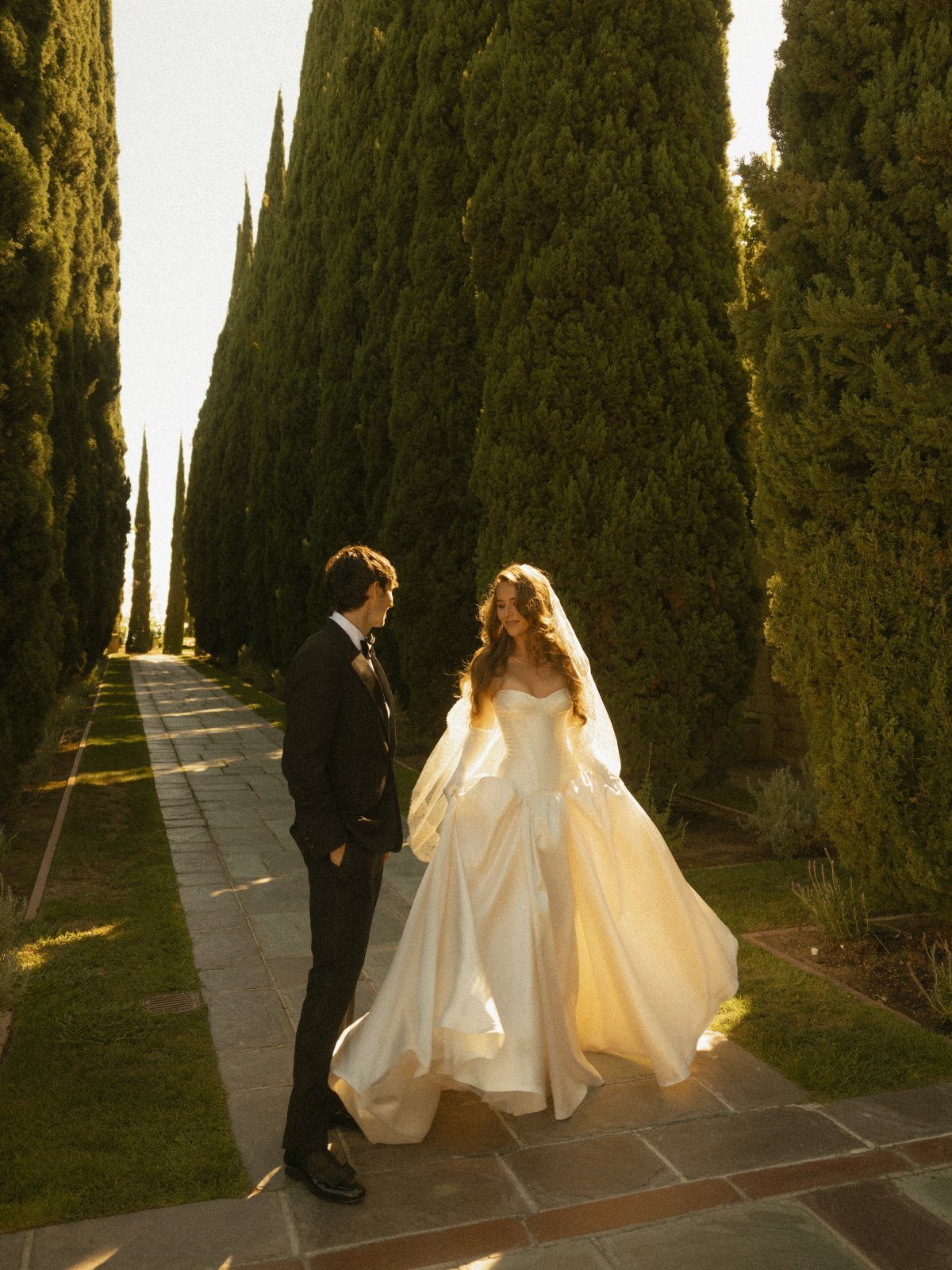 Bride and groom gazing into each other's eyes on a path with cypress trees