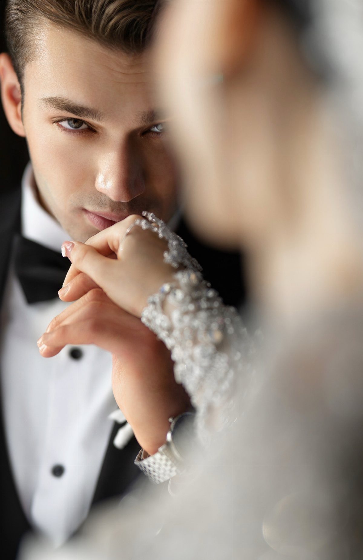 Groom in tuxedo looking at bride with her beaded sleeve near his face