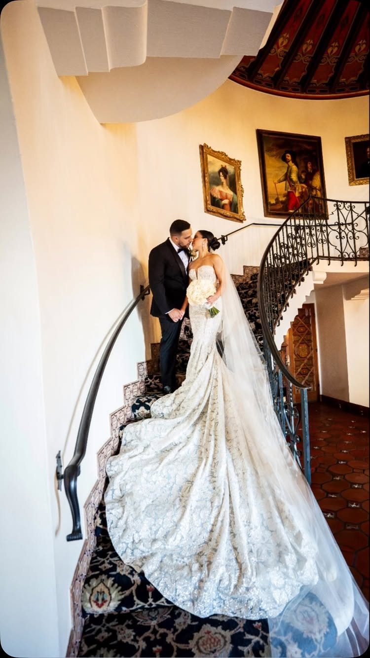 Bride and groom kissing on a grand staircase with a long white train.