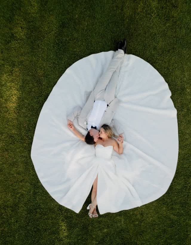 Bride and groom lying on green grass with white dress spread in circle