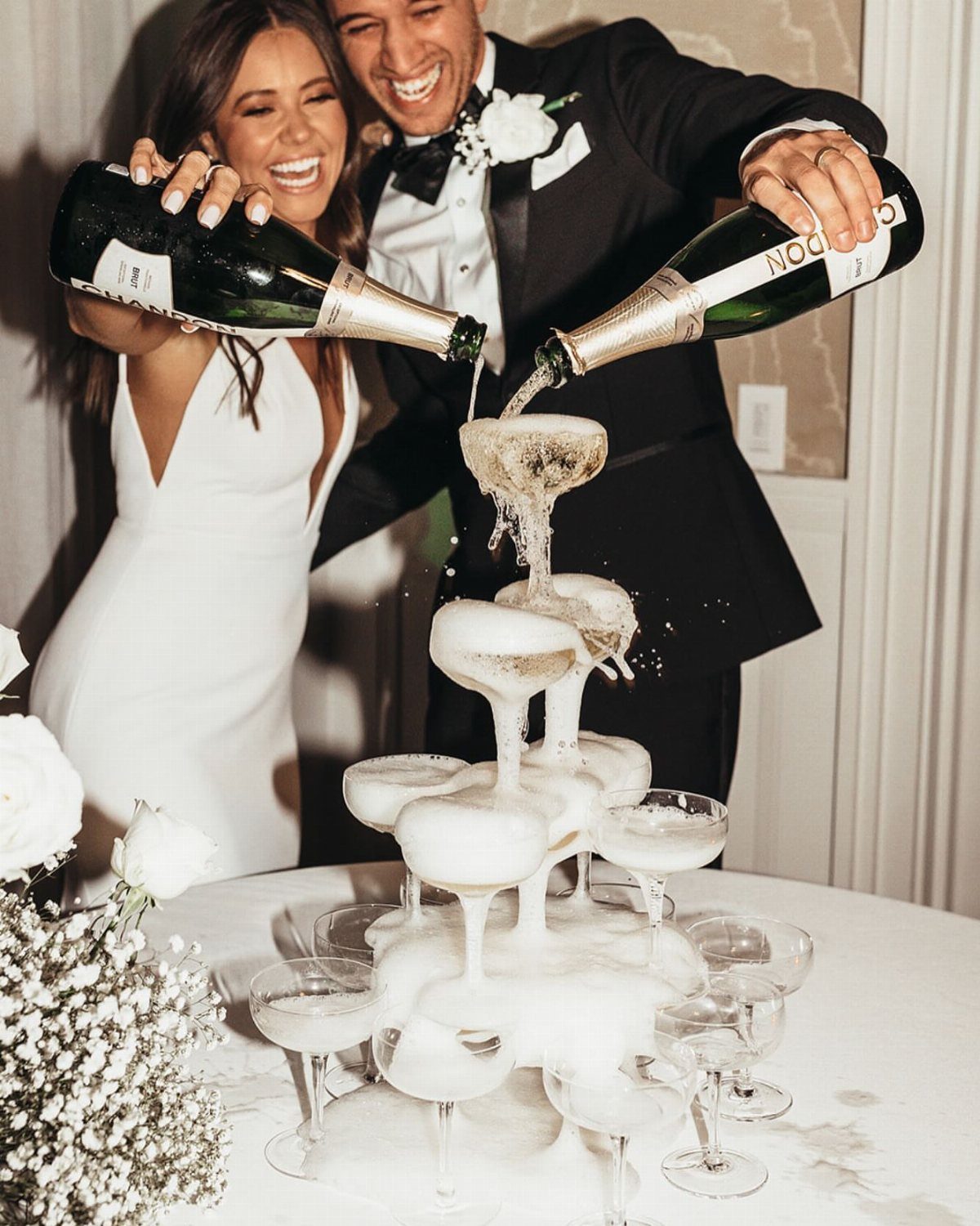 Bride and groom laughing while pouring champagne into a tiered glass tower.