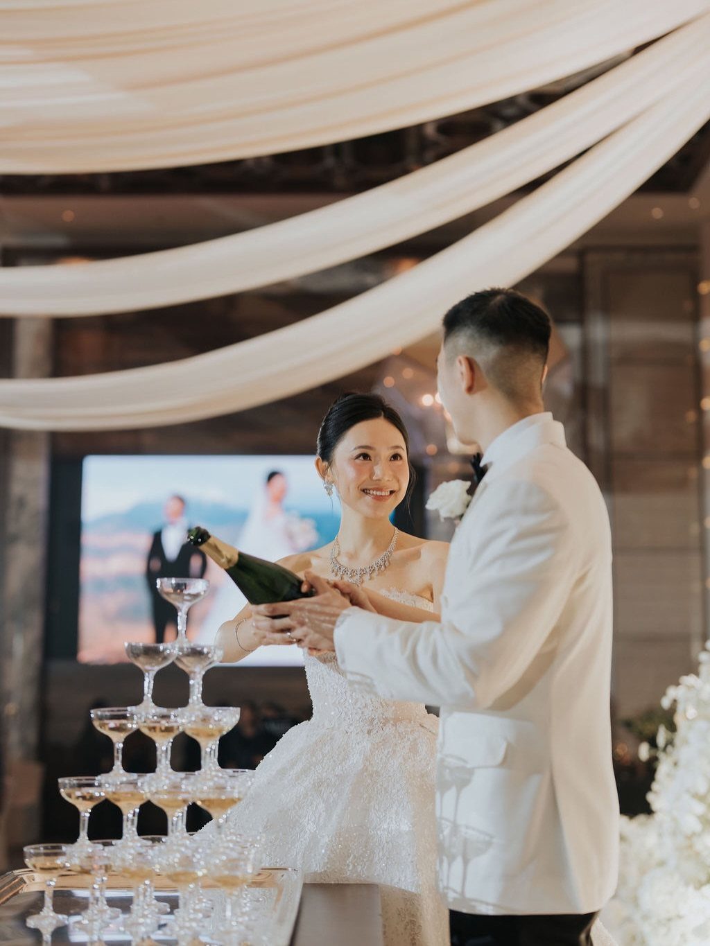 Bride and groom pouring champagne into a tower of glasses at a wedding reception
