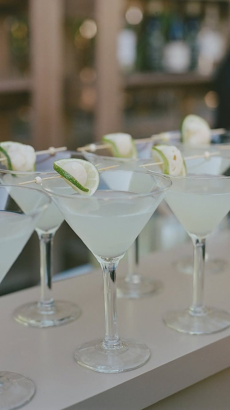 Martini glasses with pale cocktails and lime garnishes on a white table.