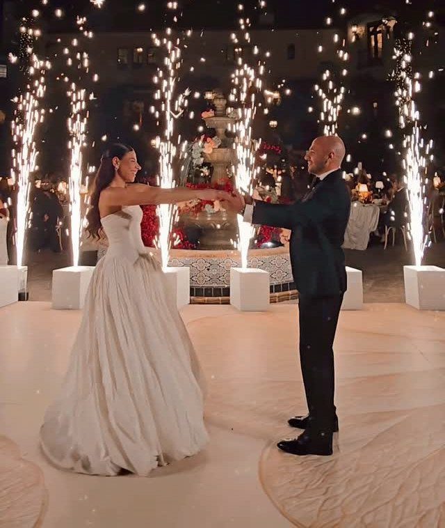 Bride and groom dancing on a white floor surrounded by bright sparkler fountains.