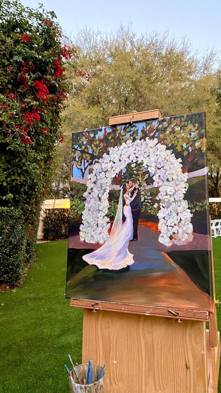 Painting of a wedding couple kissing under a floral arch on an easel