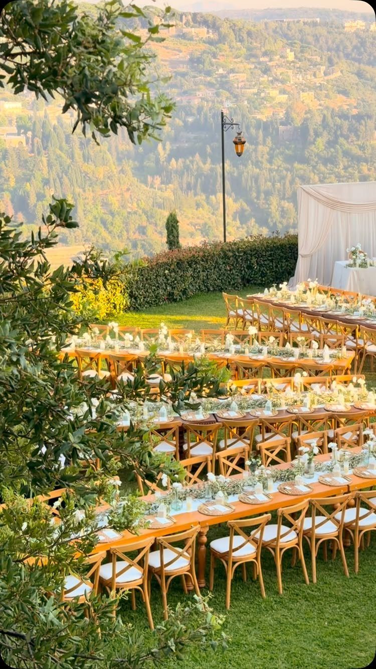Long wooden wedding tables with white settings on a lawn overlooking a valley