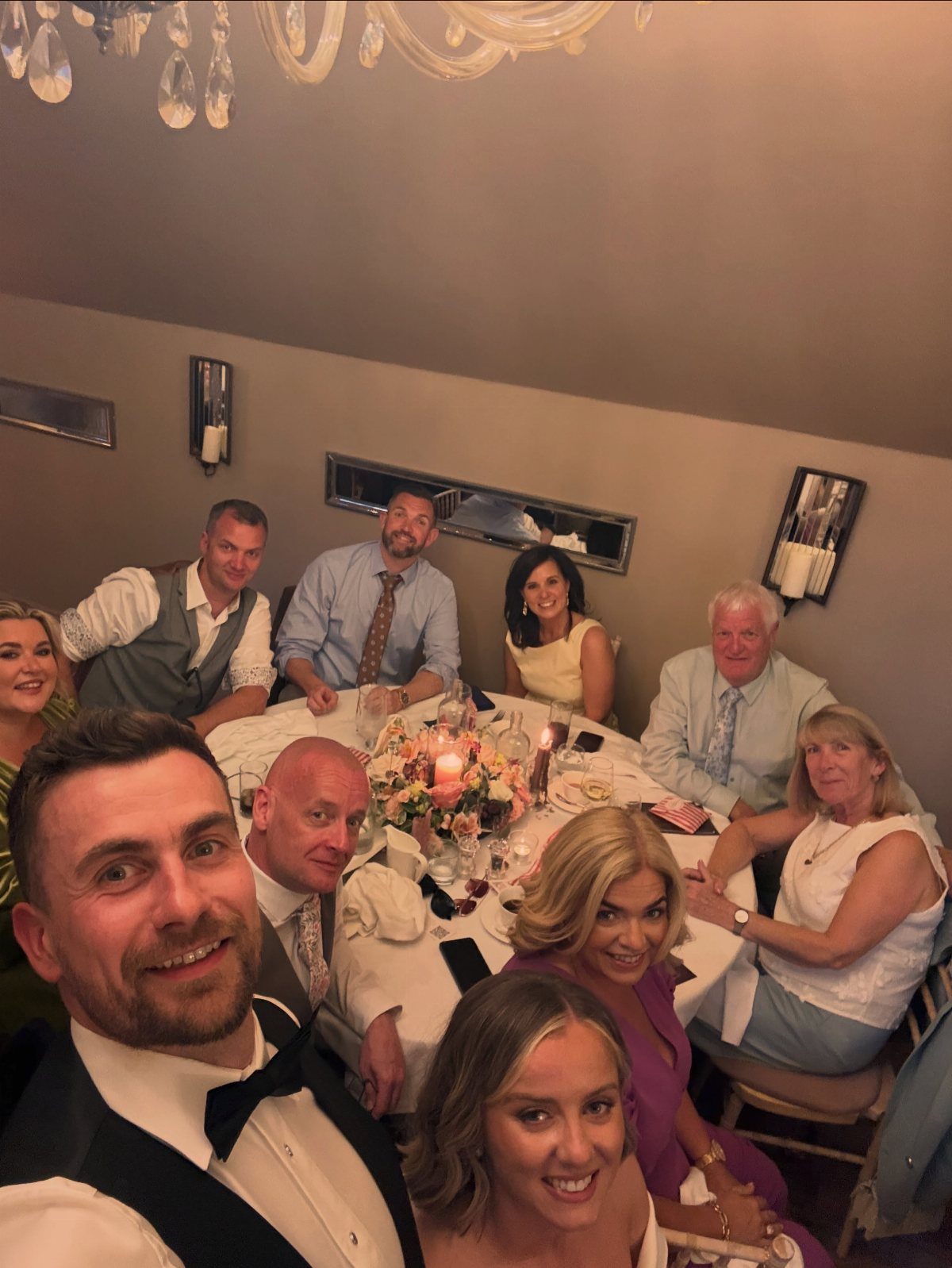 Group of wedding guests smiling for a selfie around a decorated dinner table.