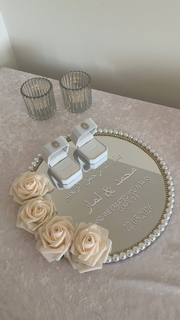 Two white ring boxes on a mirrored tray with roses and pearl edges.