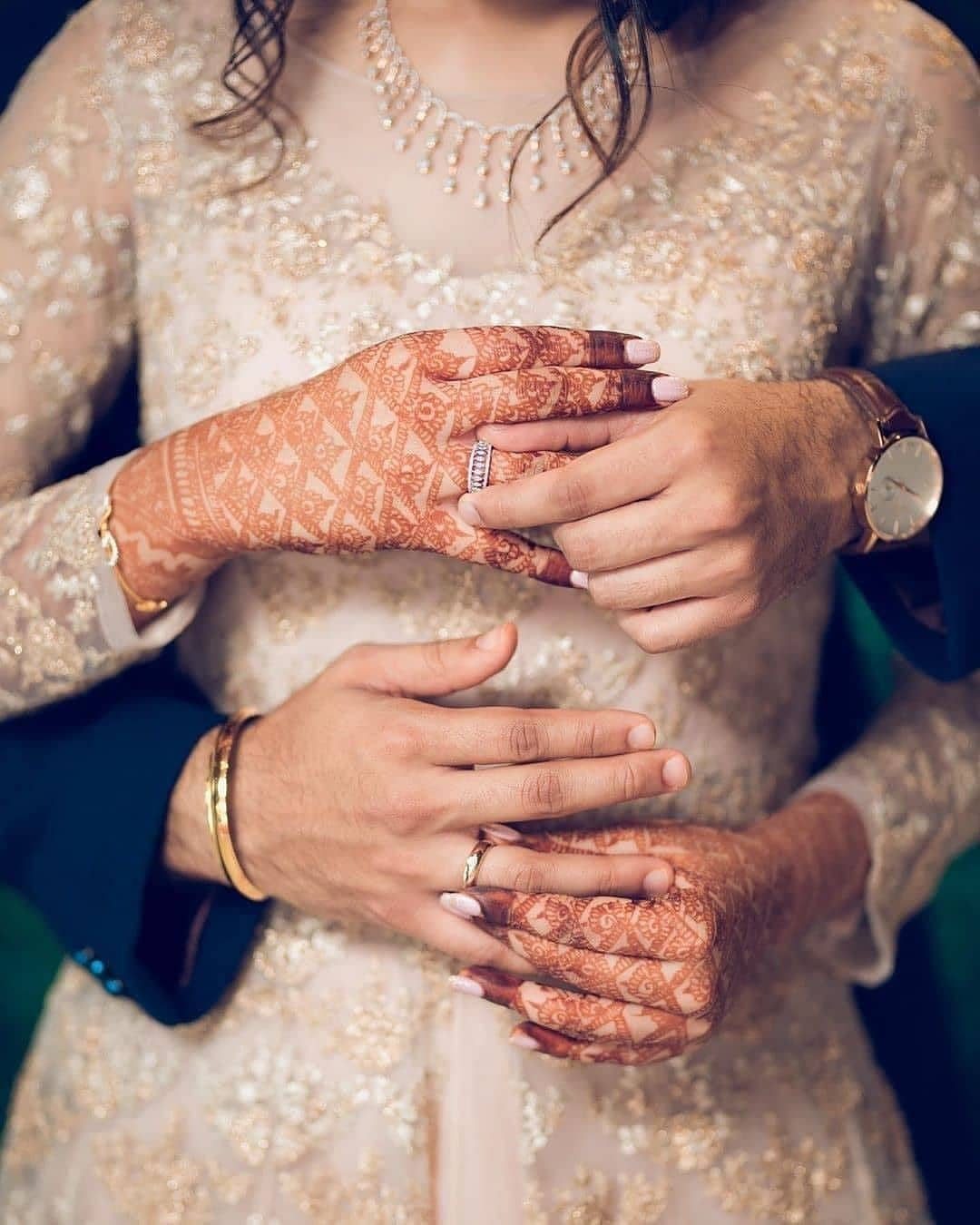 Couple's hands showing wedding rings against a cream embroidered bridal gown with henna