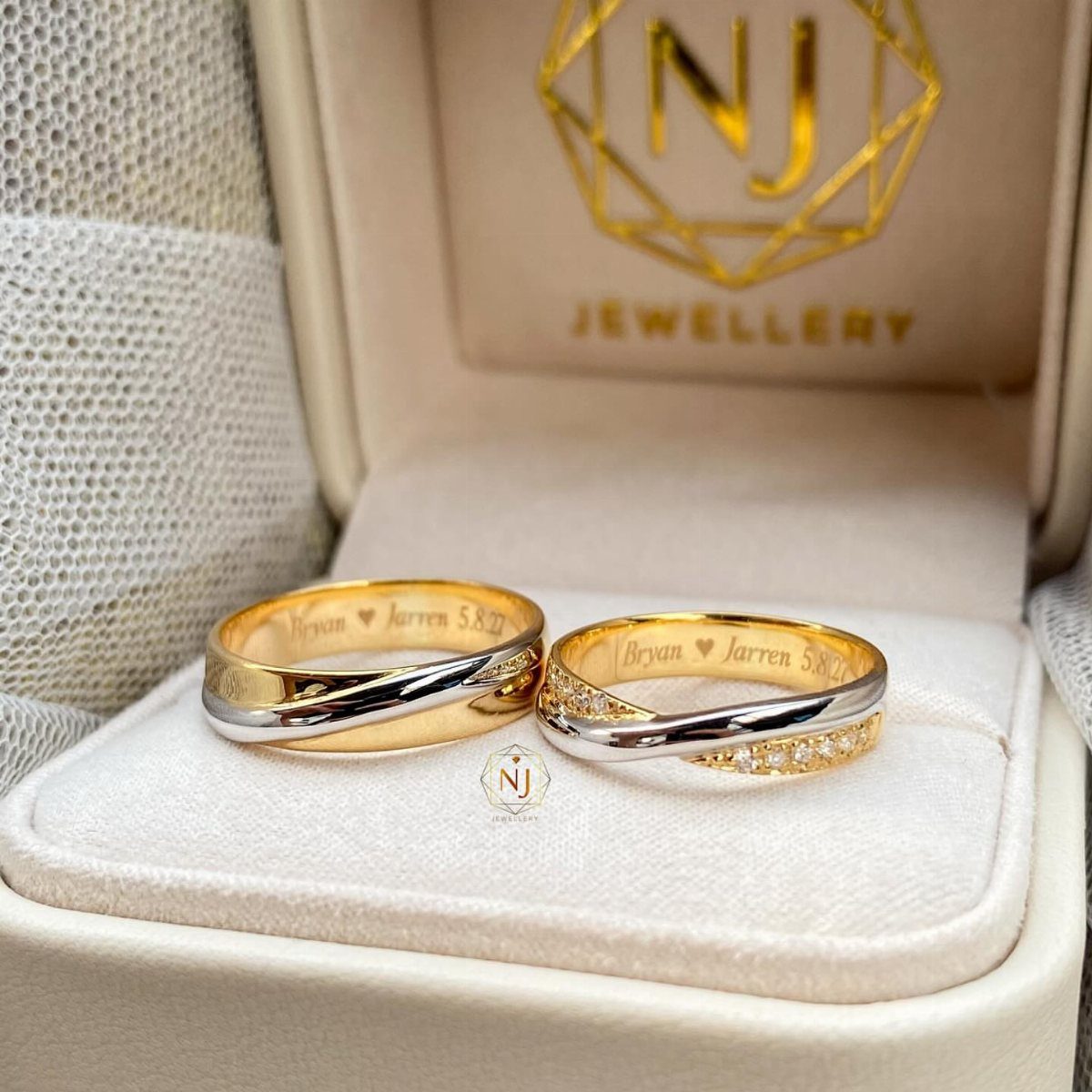 Two engraved gold and silver wedding rings resting in a white jewelry box